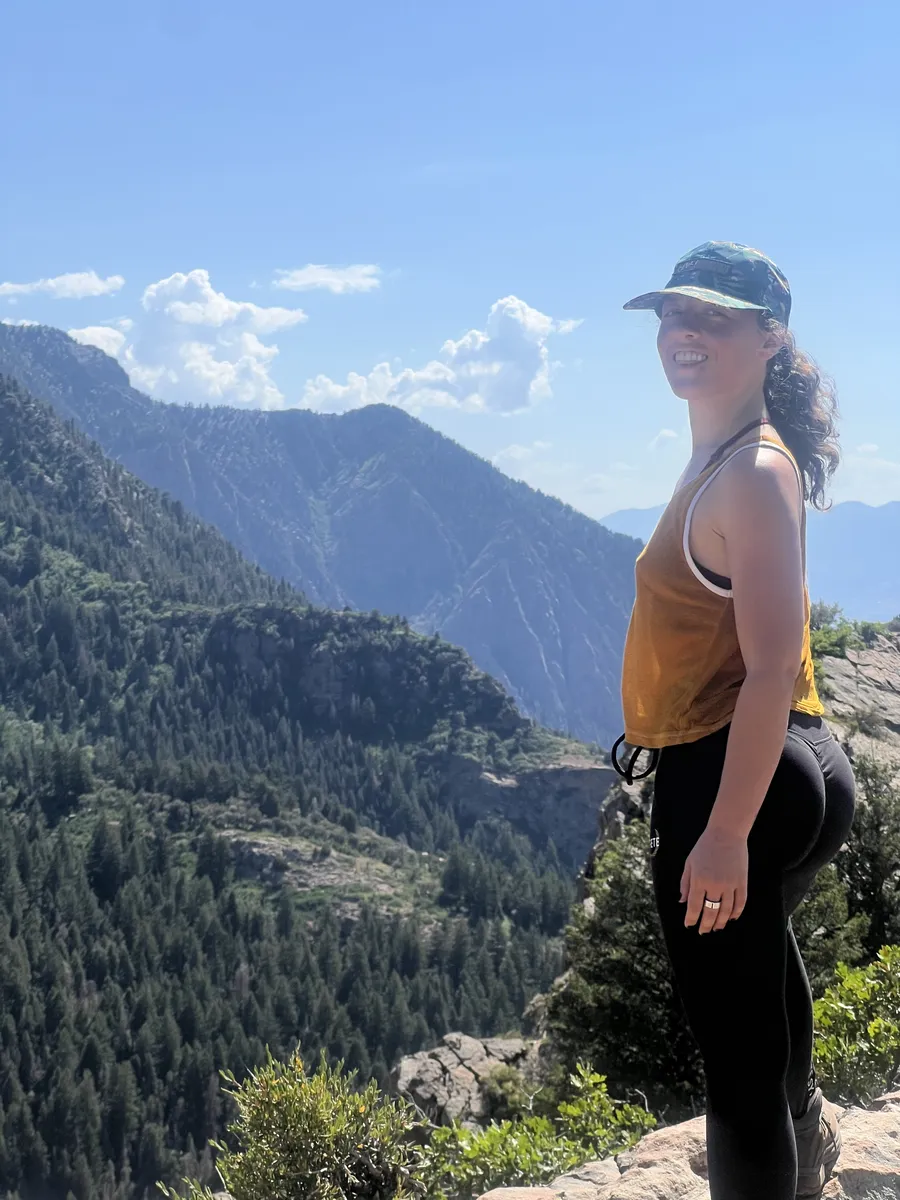 Destiny Cabrales standing above a forested mountain landscape